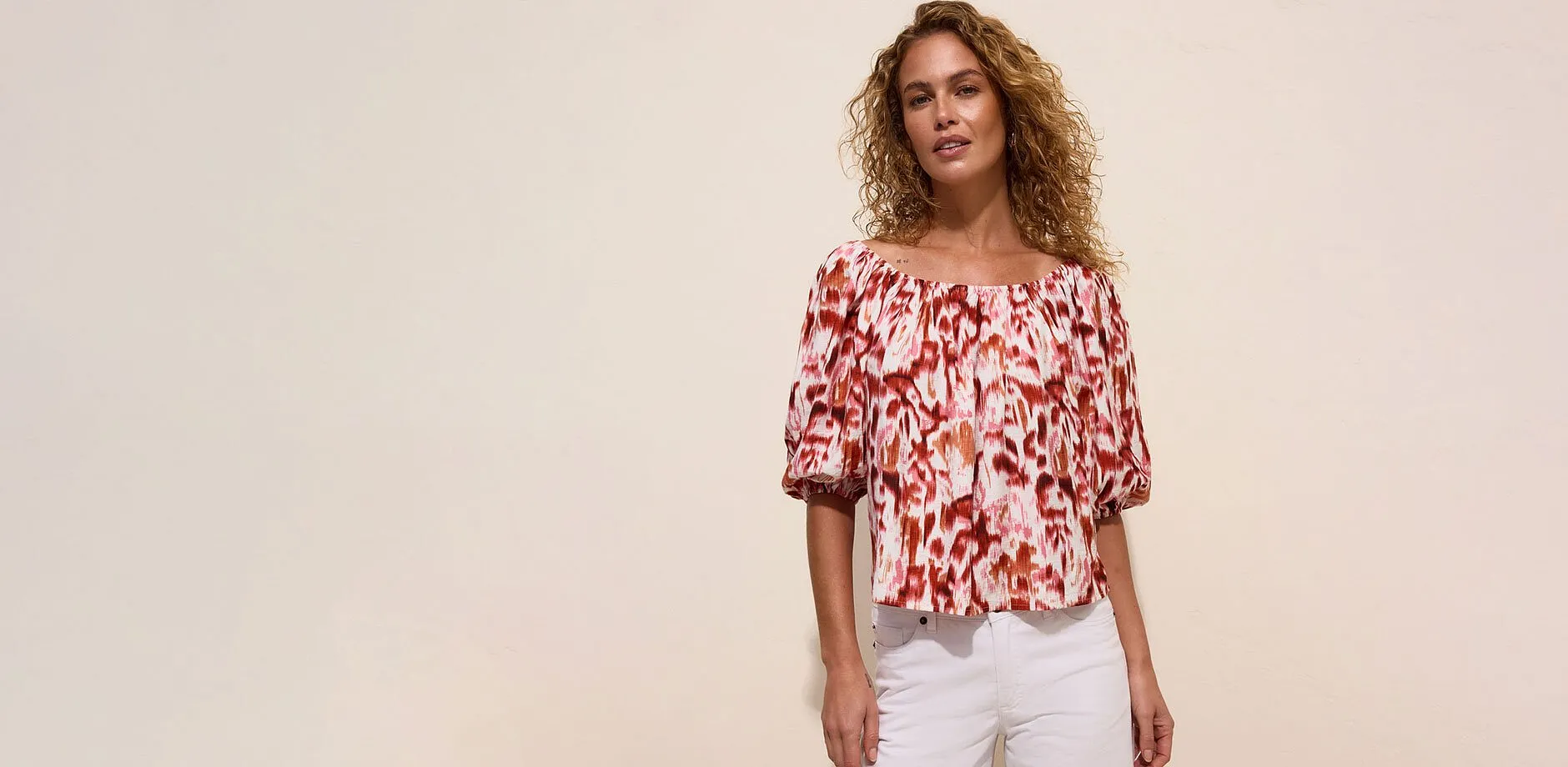 Una blusa con spalle scoperte con una fantasia vivace e comodi jeans bianchi.