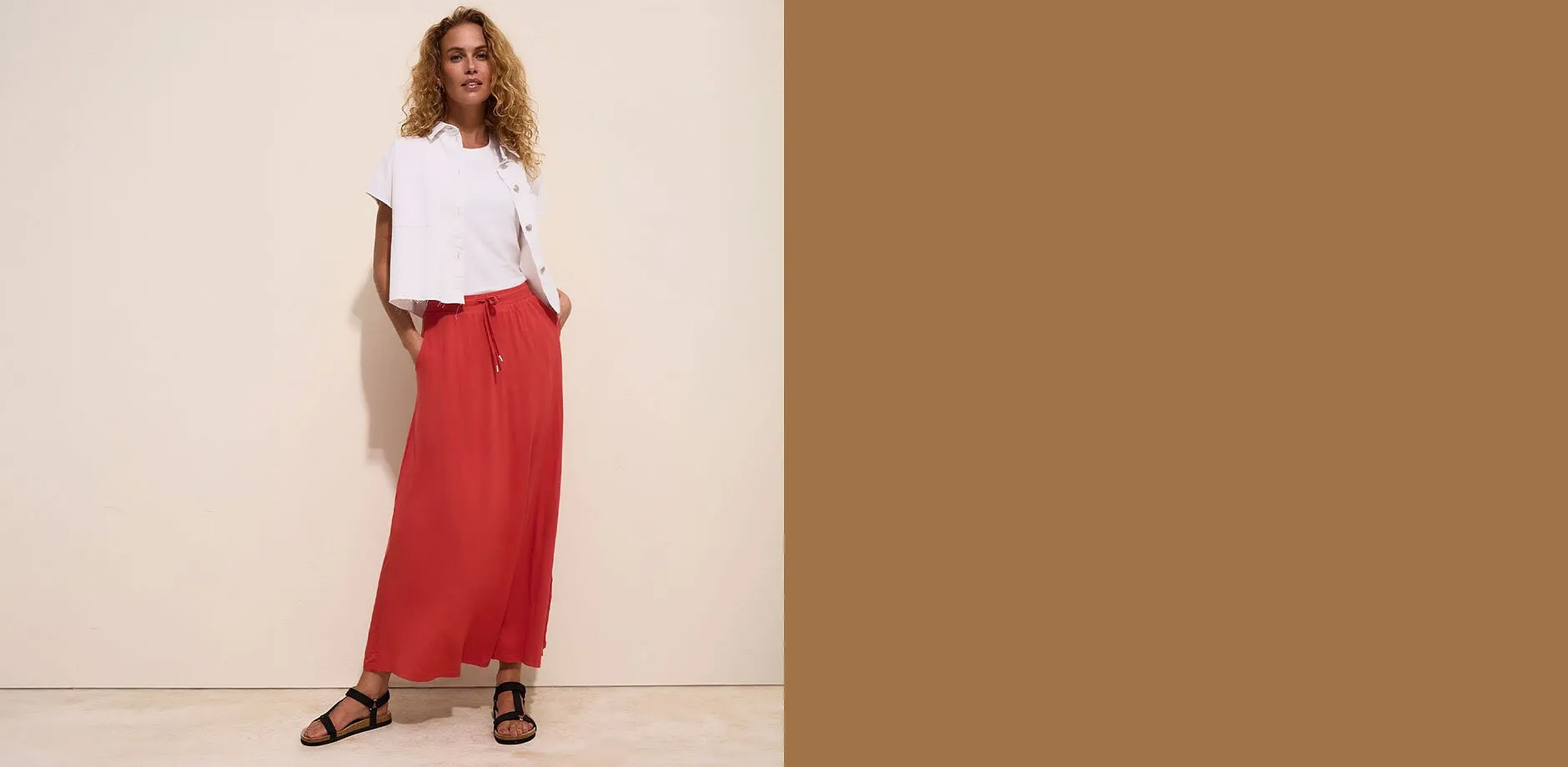 Una camicetta bianca dal taglio disinvolto, una maglietta bianca, una gonna lunga rossa e dei sandali neri.