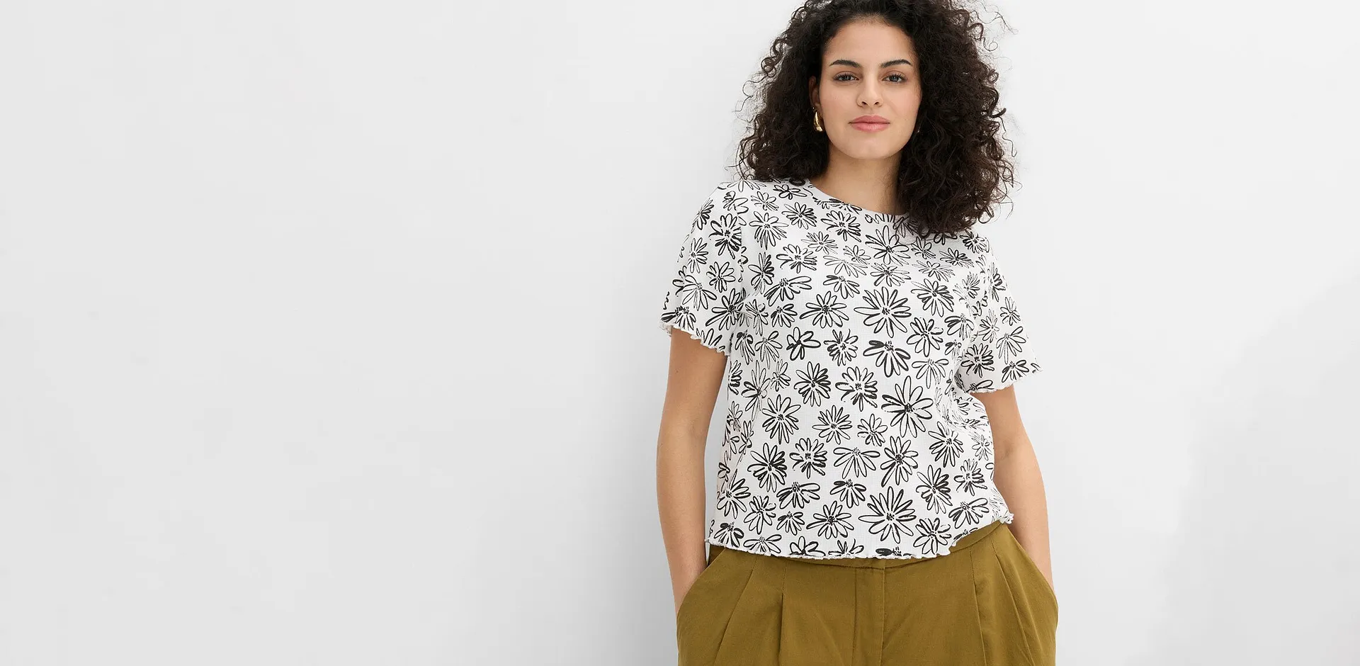 Maglia bianca con motivi neri e pantaloni verde oliva.