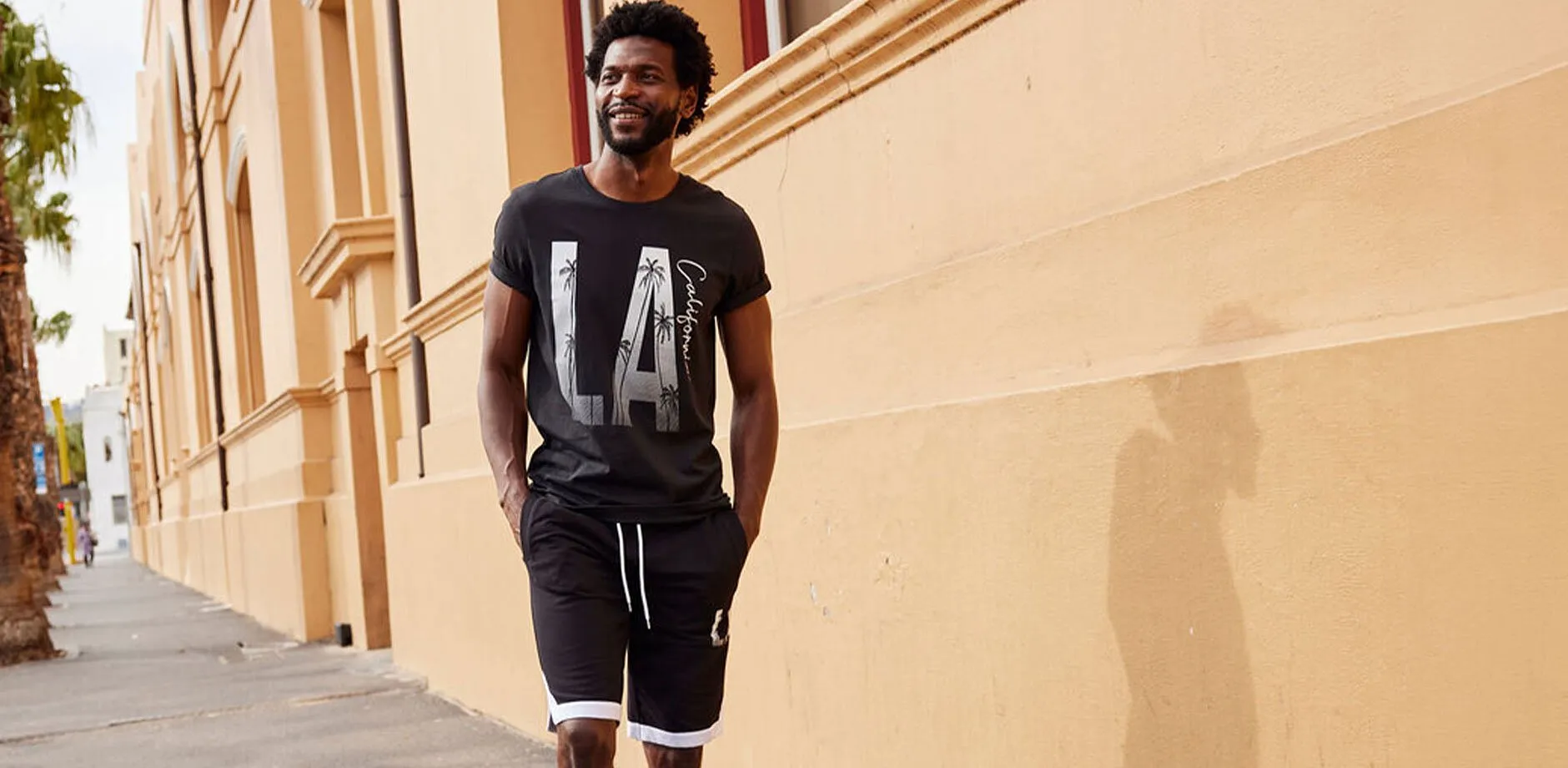 Uomo vestito in modo disinvolto con una maglietta nera con la scritta &laquo;LA&raquo; e pantaloni corti abbinati.
