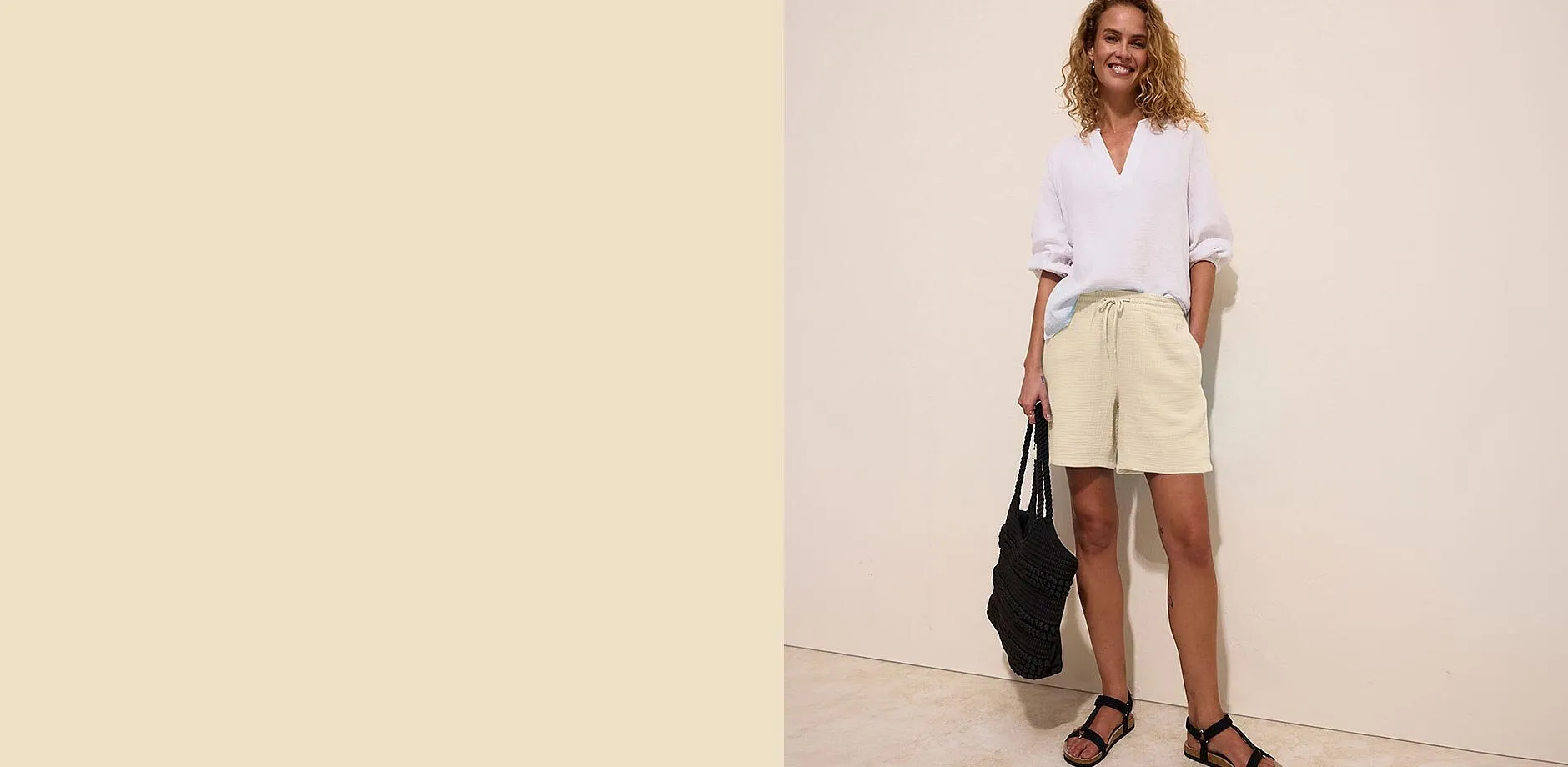 Blusa bianca, pantaloncini di mussola beige e sandali neri per un look estivo disinvolto.