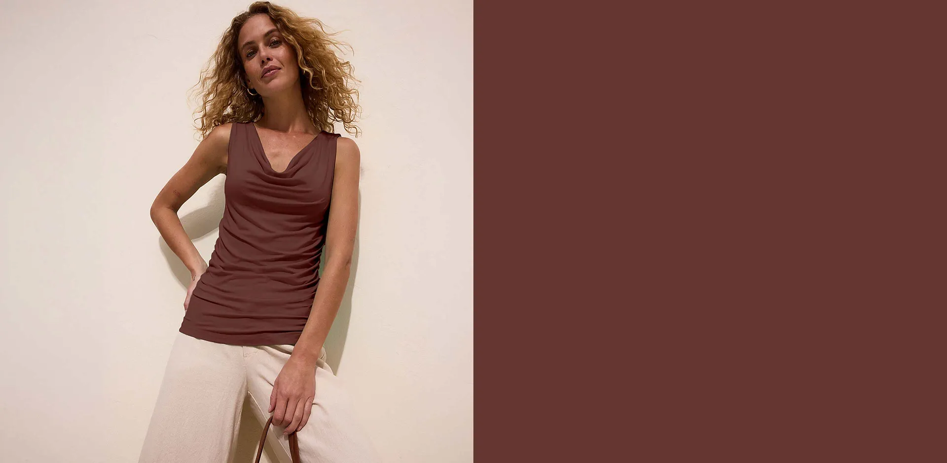 Top marrone con scollo a cascata, abbinato a pantaloni chiari dal taglio ampio.