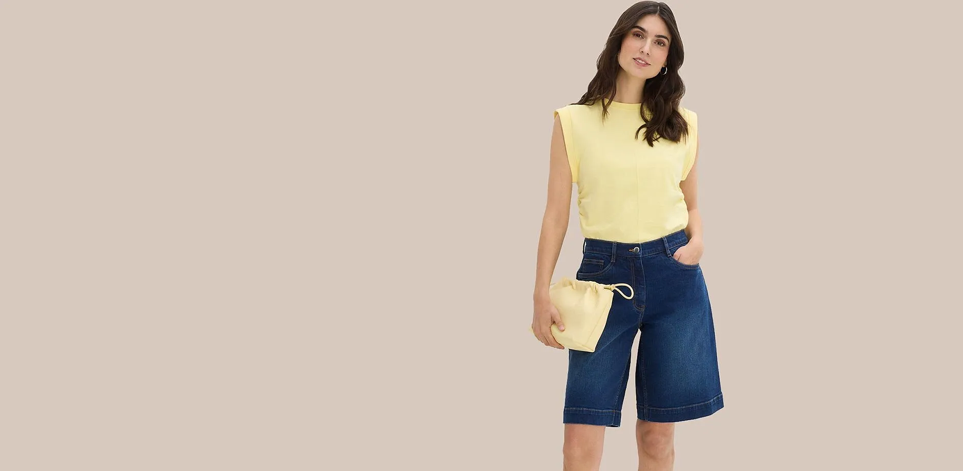 Top giallo con spalline imbottite, bermuda blu in jeans e borsa a sacchetto abbinata.
