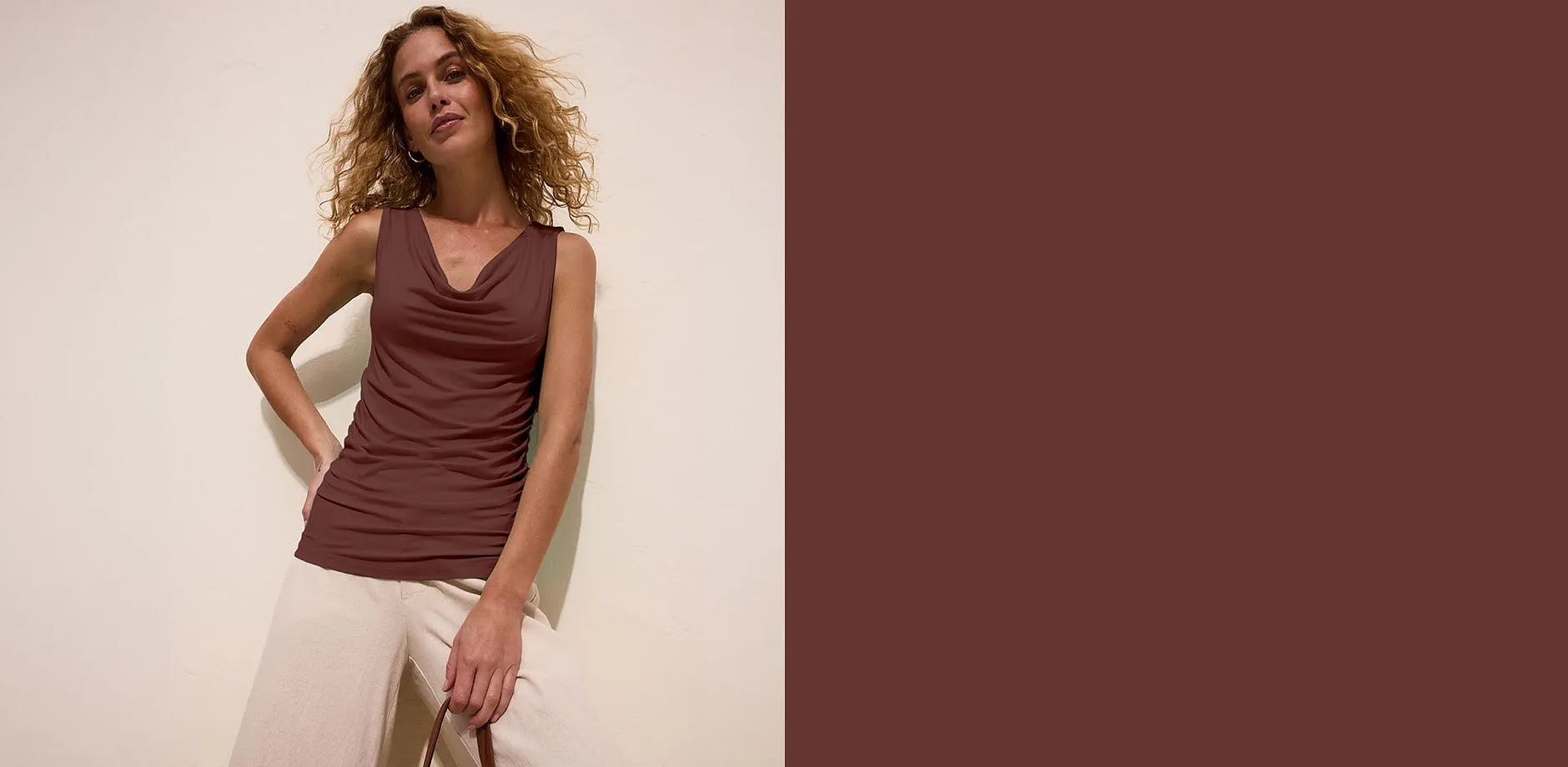 Top marrone con scollo a cascata, abbinato a pantaloni chiari dal taglio ampio.
