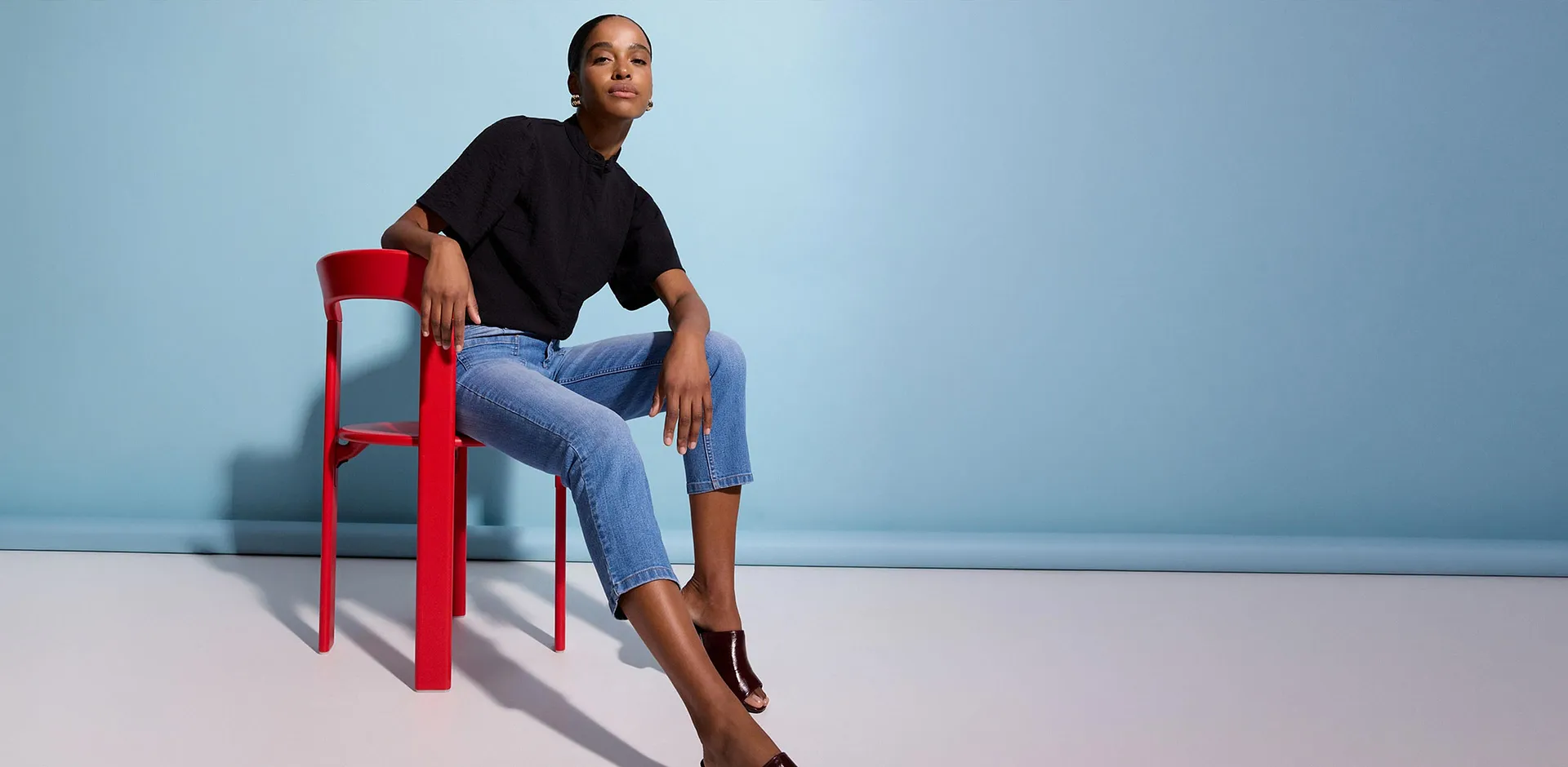 Outfit composto da maglia nera, jeans blu e mules lucide.