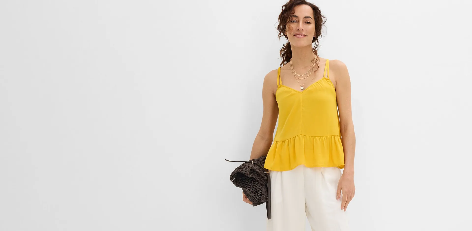 Canotta gialla, pantaloni bianchi larghi e una borsa marrone.