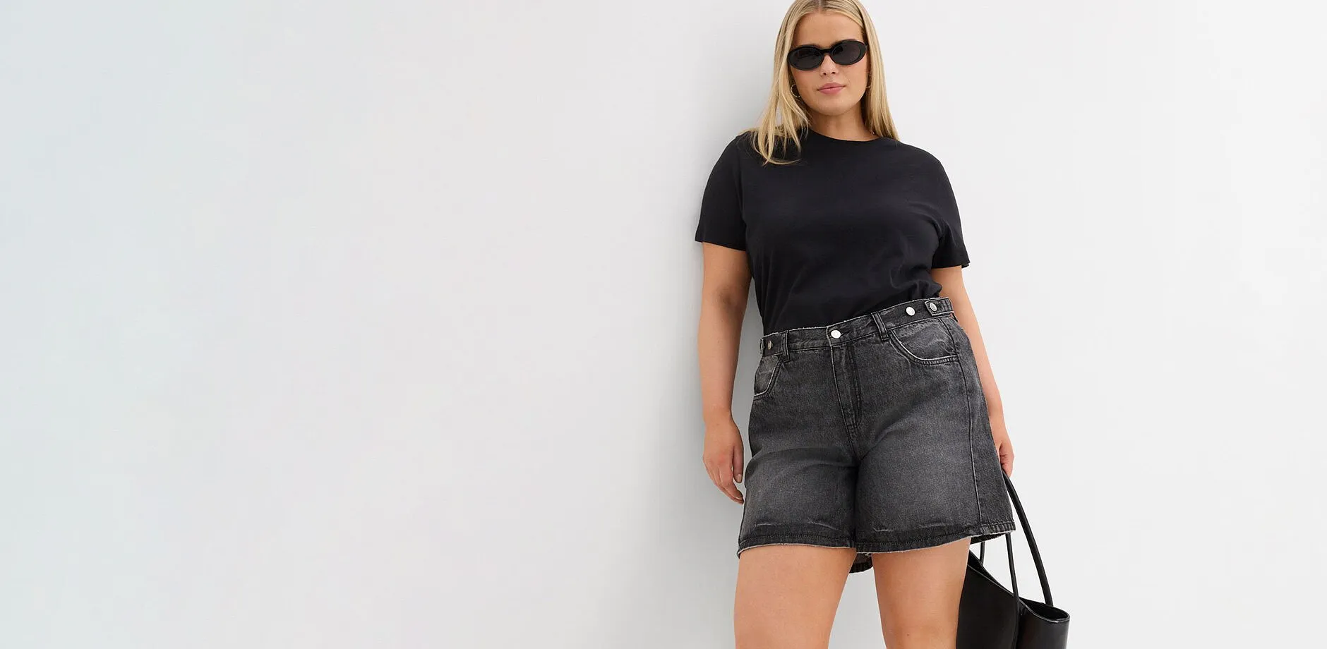  Maglietta nera, pantaloncini larghi di jeans grigi, occhiali da sole e borsa nera.