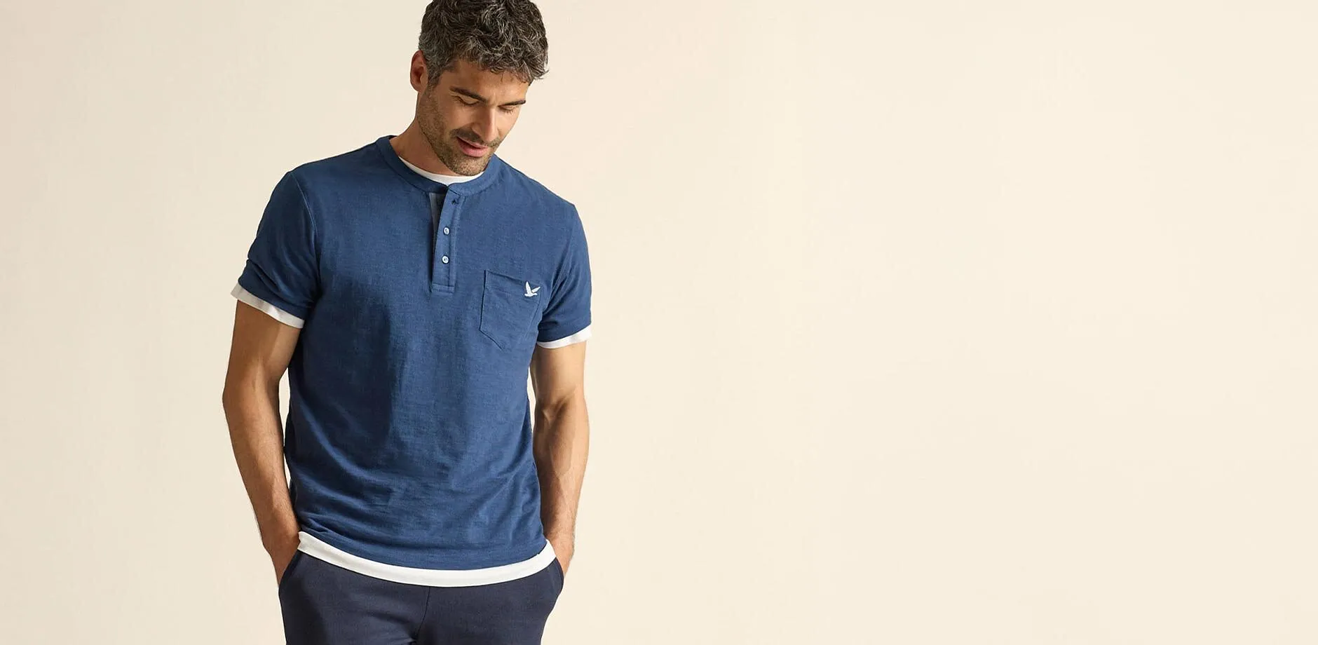 Maglia serafino blu casual con dettagli bianchi, maglietta bianca sotto e pantaloni scuri.