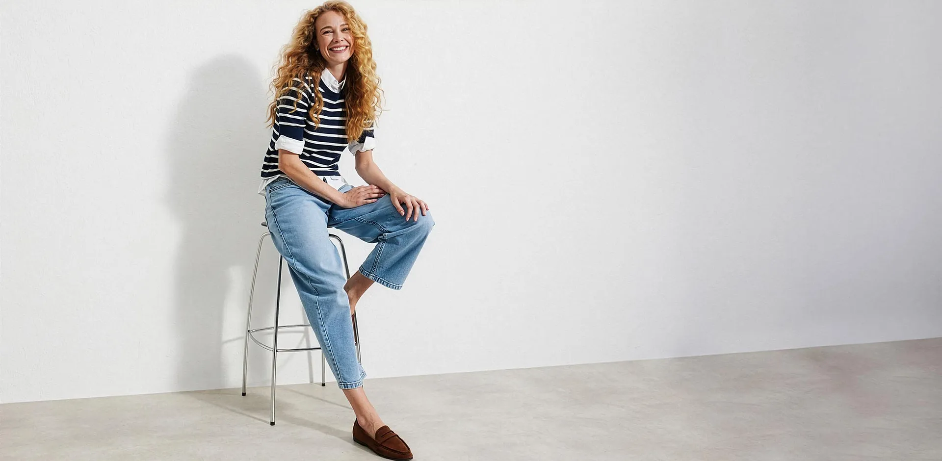 Maglione a righe sopra una camicetta, jeans chiari e mocassini marroni.