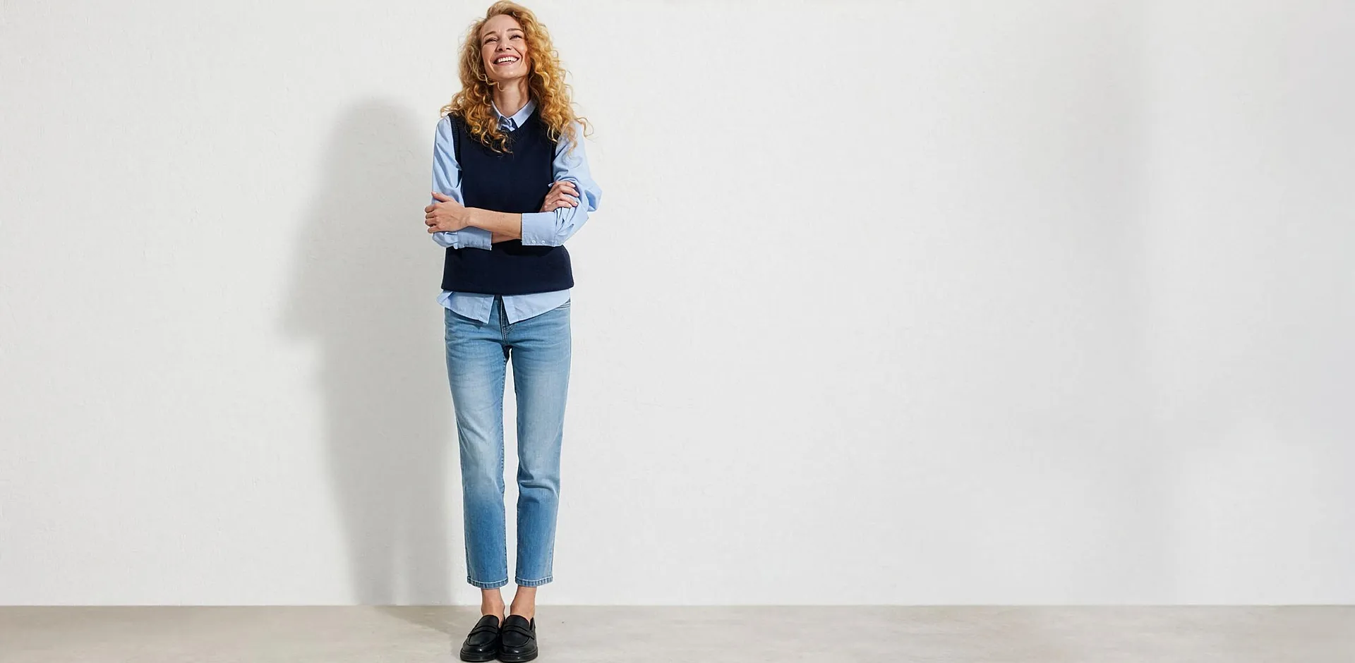 Camicia azzurra, gilet blu scuro, jeans blu e mocassini neri.