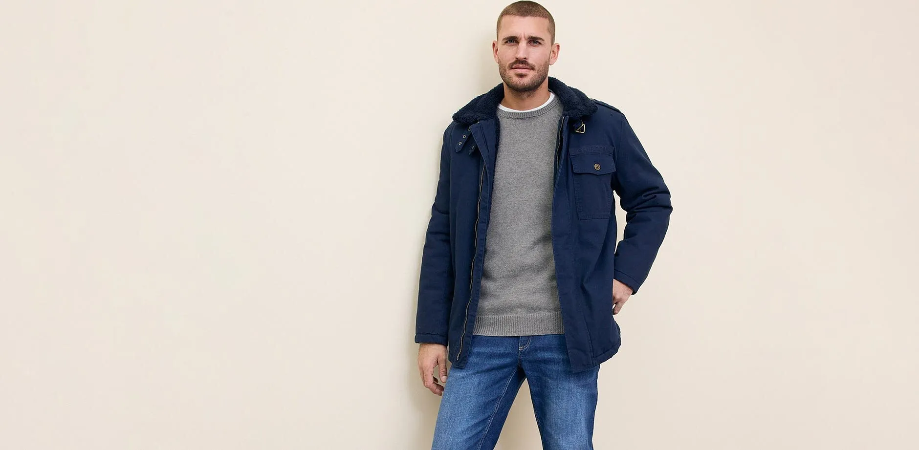 Giacca blu scuro sopra un maglione grigio, abbinata a jeans blu.