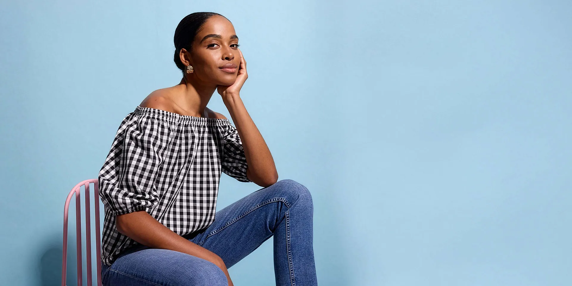 Una donna indossa una camicetta con spalle scoperte bianca e nera a quadri e dei jeans blu.