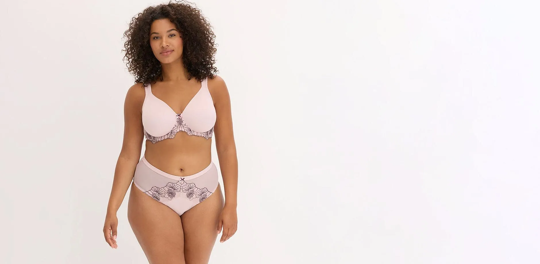 Lingerie rosa chiaro con delicati ricami floreali neri sul reggiseno e sulle mutandine.