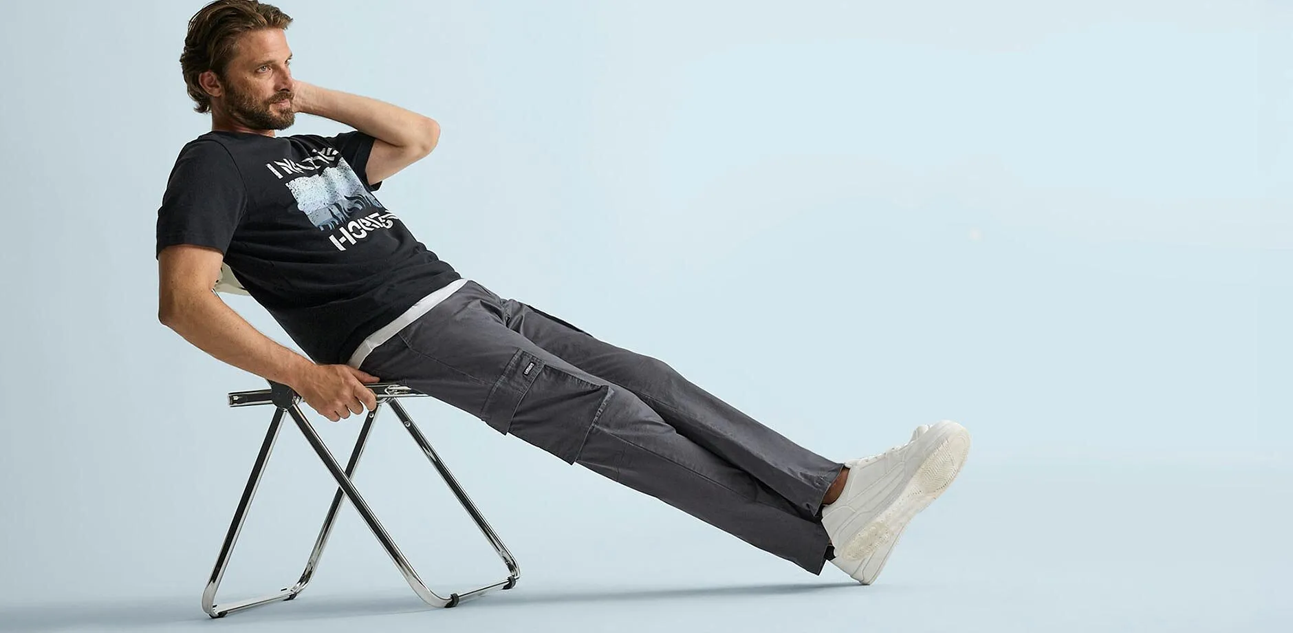 Maglietta nera con stampa, comodi pantaloni cargo grigi e sneaker bianche dal look casual.
