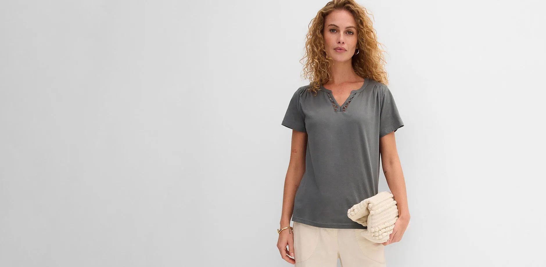 Maglietta grigia con scollo a V, pantaloni chiari e pochette beige testurizzata.