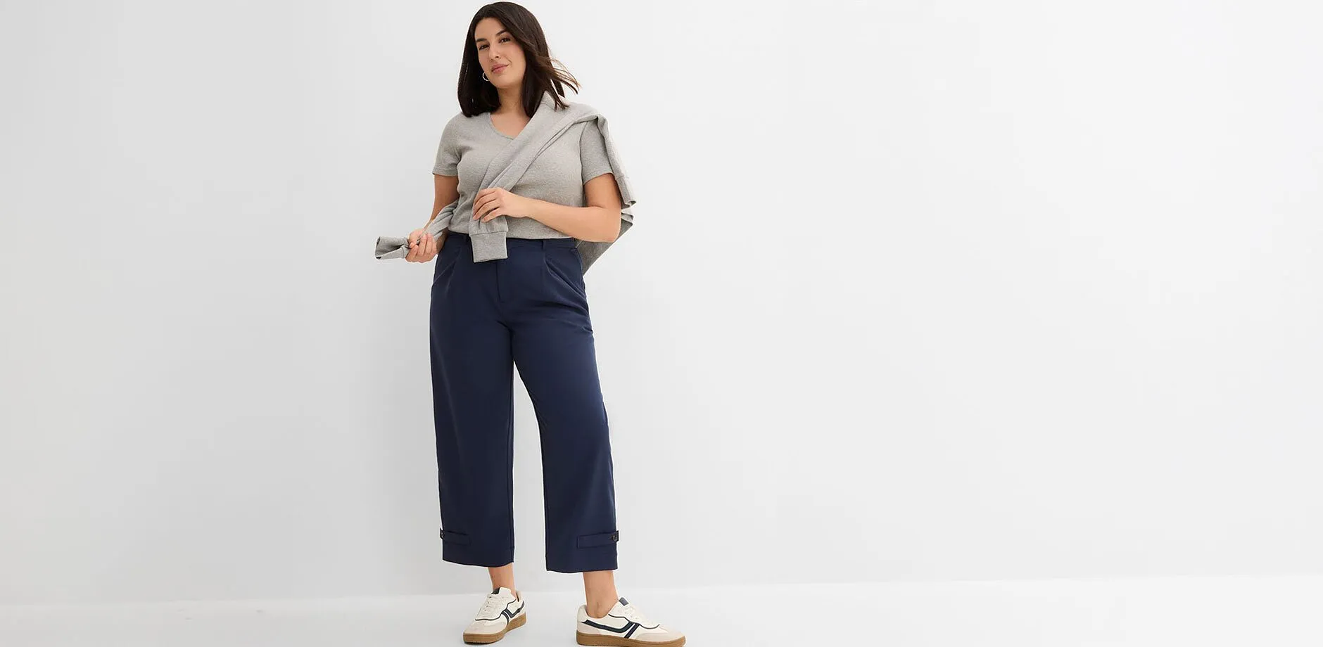 Maglietta grigia, pantaloni blu navy, maglione, sneaker bianche.