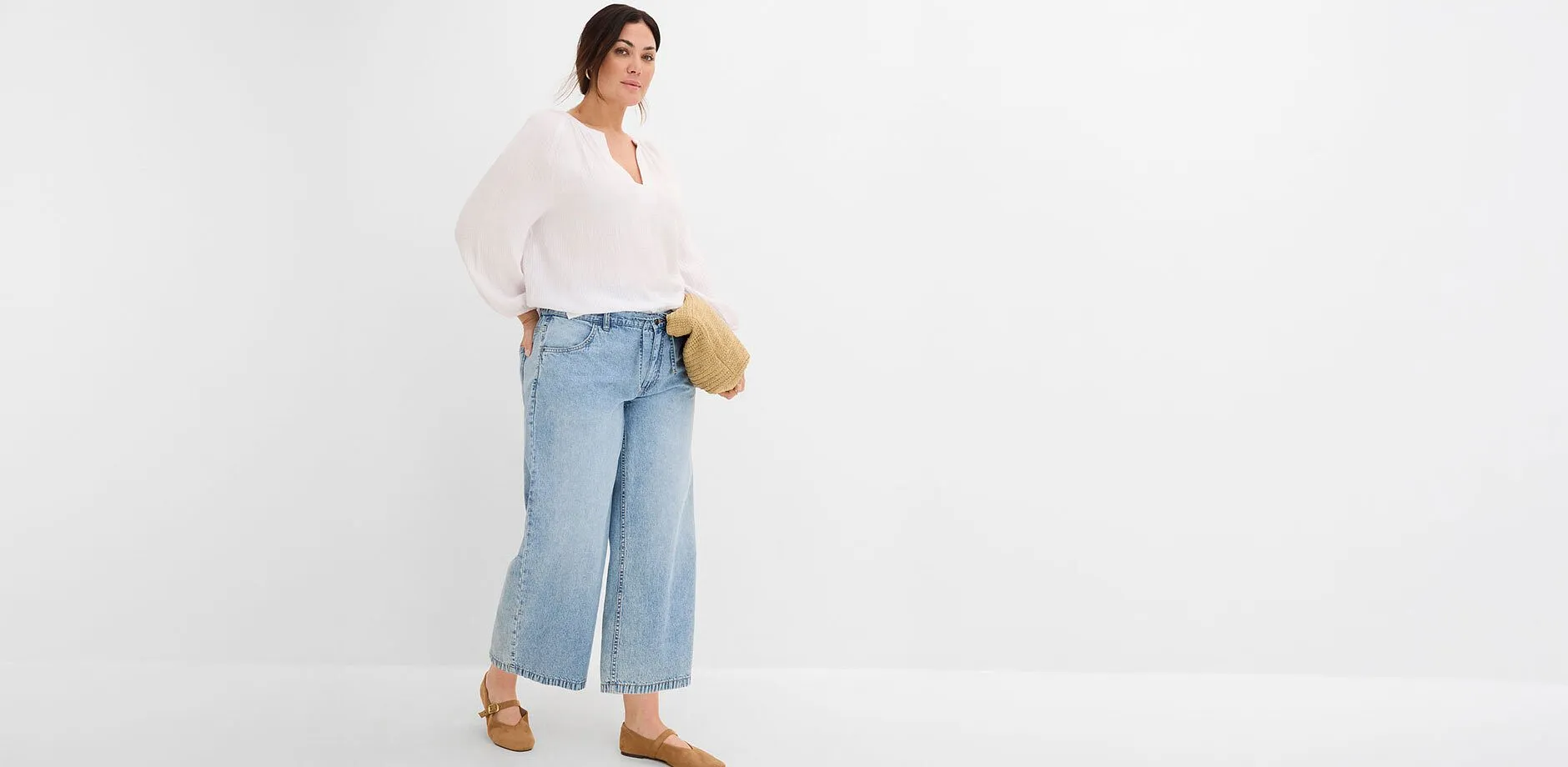 Una camicetta bianca ampia, jeans larghi, abbinati a scarpe marroni e una borsa intrecciata.