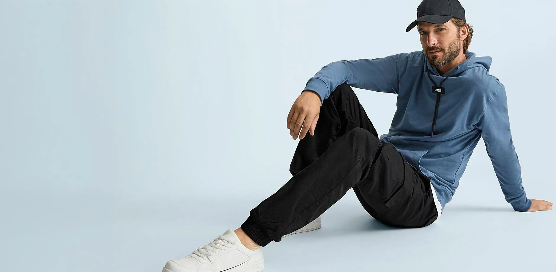 Giacca blu con cappuccio, pantaloni cargo neri, scarpe da ginnastica bianche e berretto nero per un look casual.