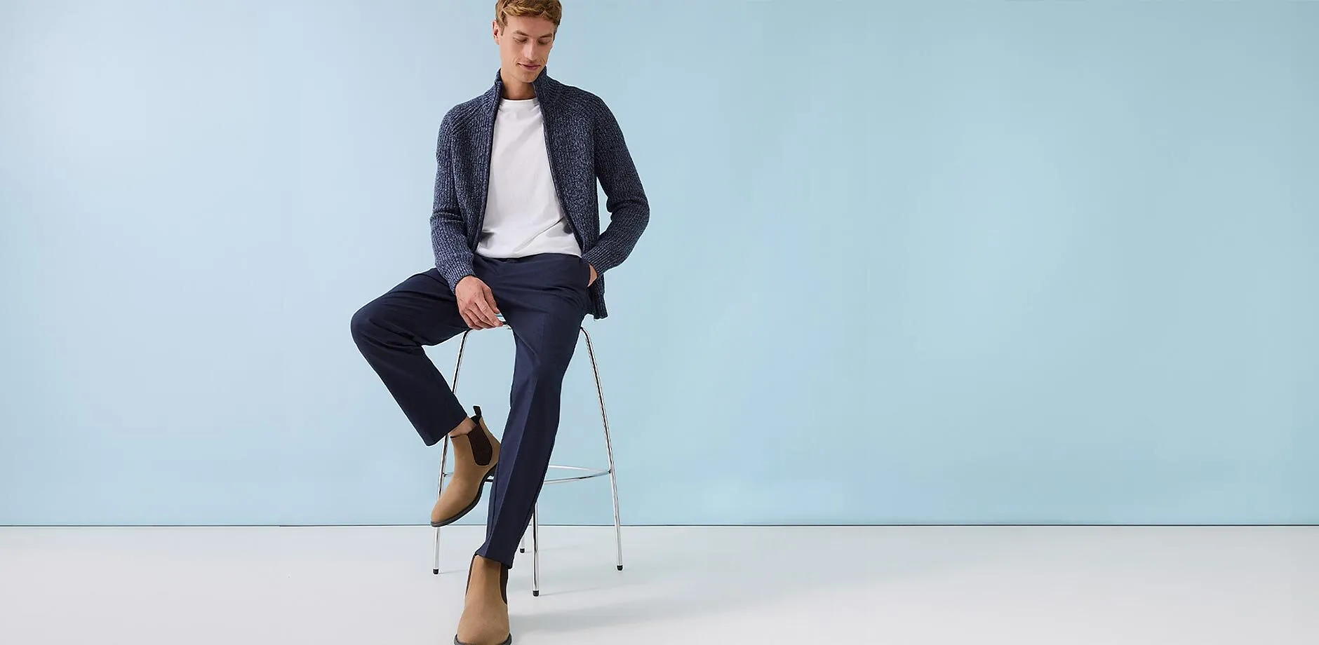 Cardigan blu scuro sopra una maglietta bianca, abbinato a pantaloni eleganti e stivaletti in camoscio beige.