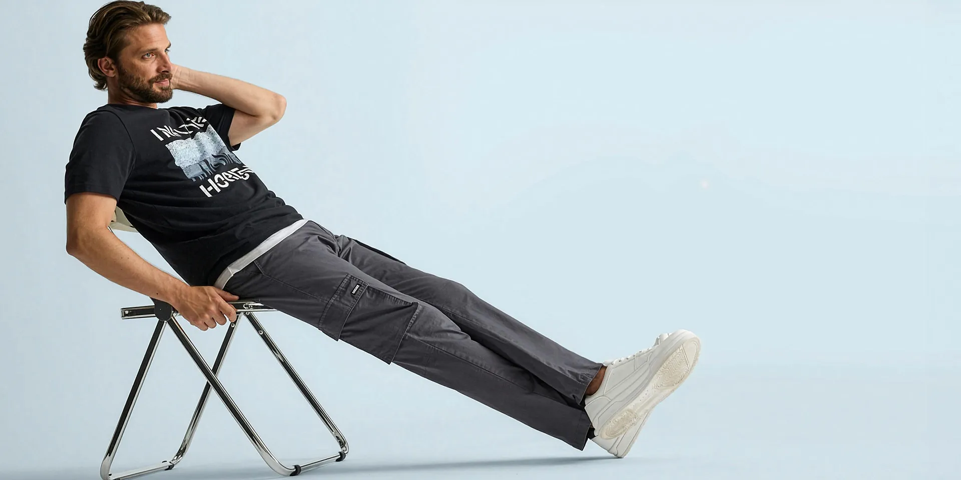 Maglietta nera con stampa, comodi pantaloni cargo grigi e sneaker bianche dal look casual.
