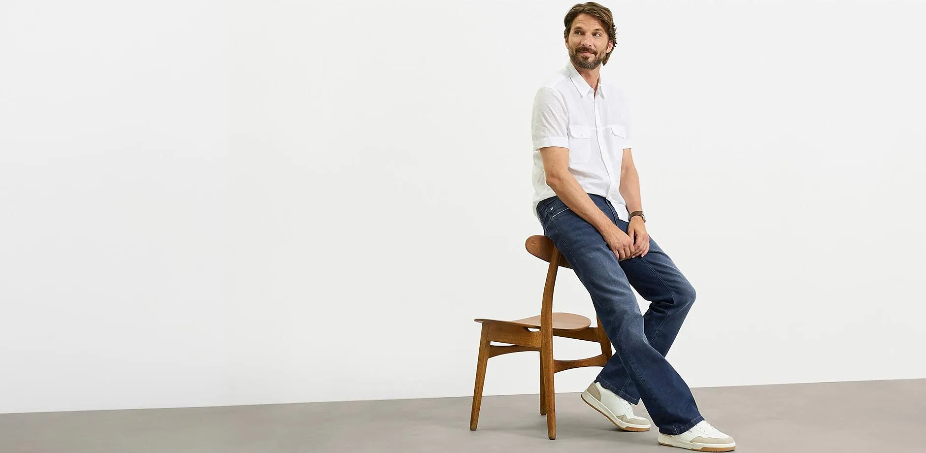 Camicia bianca a maniche corte, jeans scuri e sneaker bianche per un look casual.