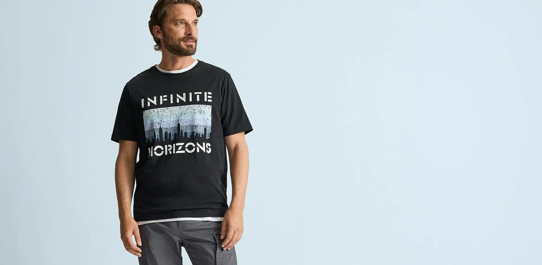 Maglietta nera con la scritta &ldquo;Infinite Horizons&rdquo; e pantaloni cargo grigi dal look casual.