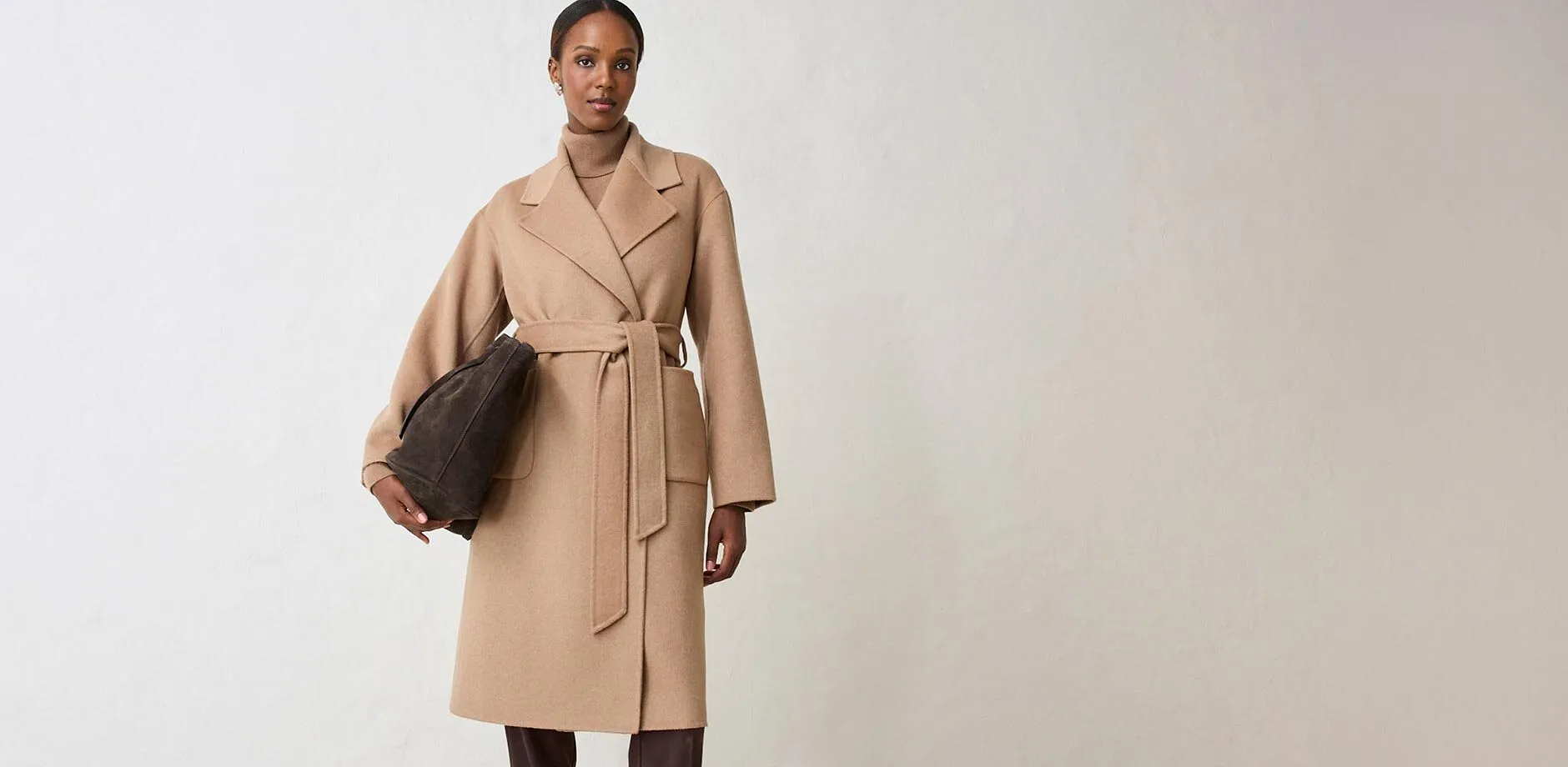 Elegante cappotto avvolgente color beige, con sotto un maglione a collo alto, completato da una borsa scura.