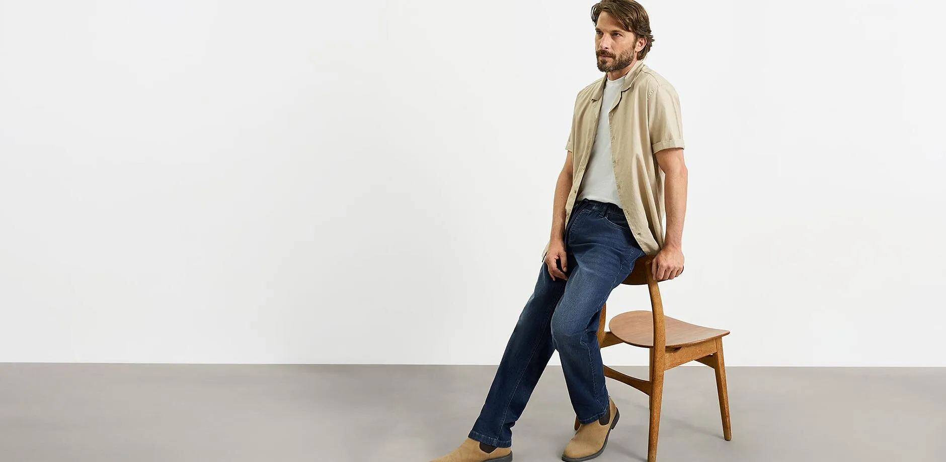 Camicia beige, maglietta grigia, jeans blu e scarpe di camoscio marroni.