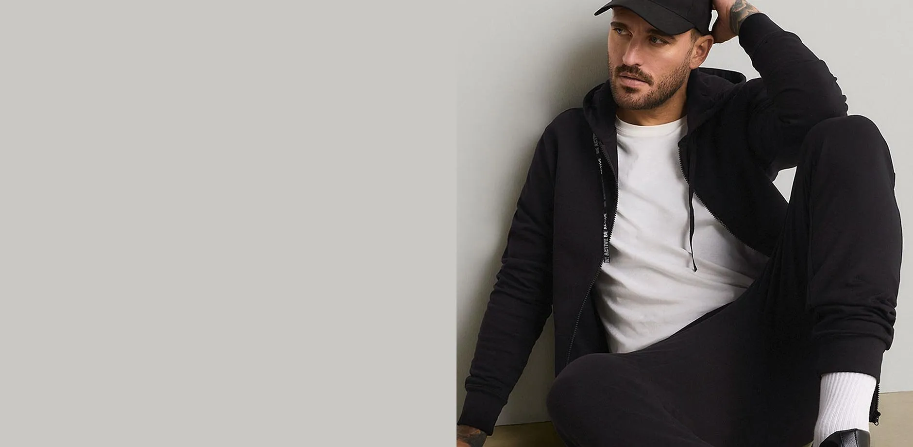 Un berretto nero, una felpa con cappuccio, una maglietta bianca e dei pantaloni da jogging neri creano un look casual.