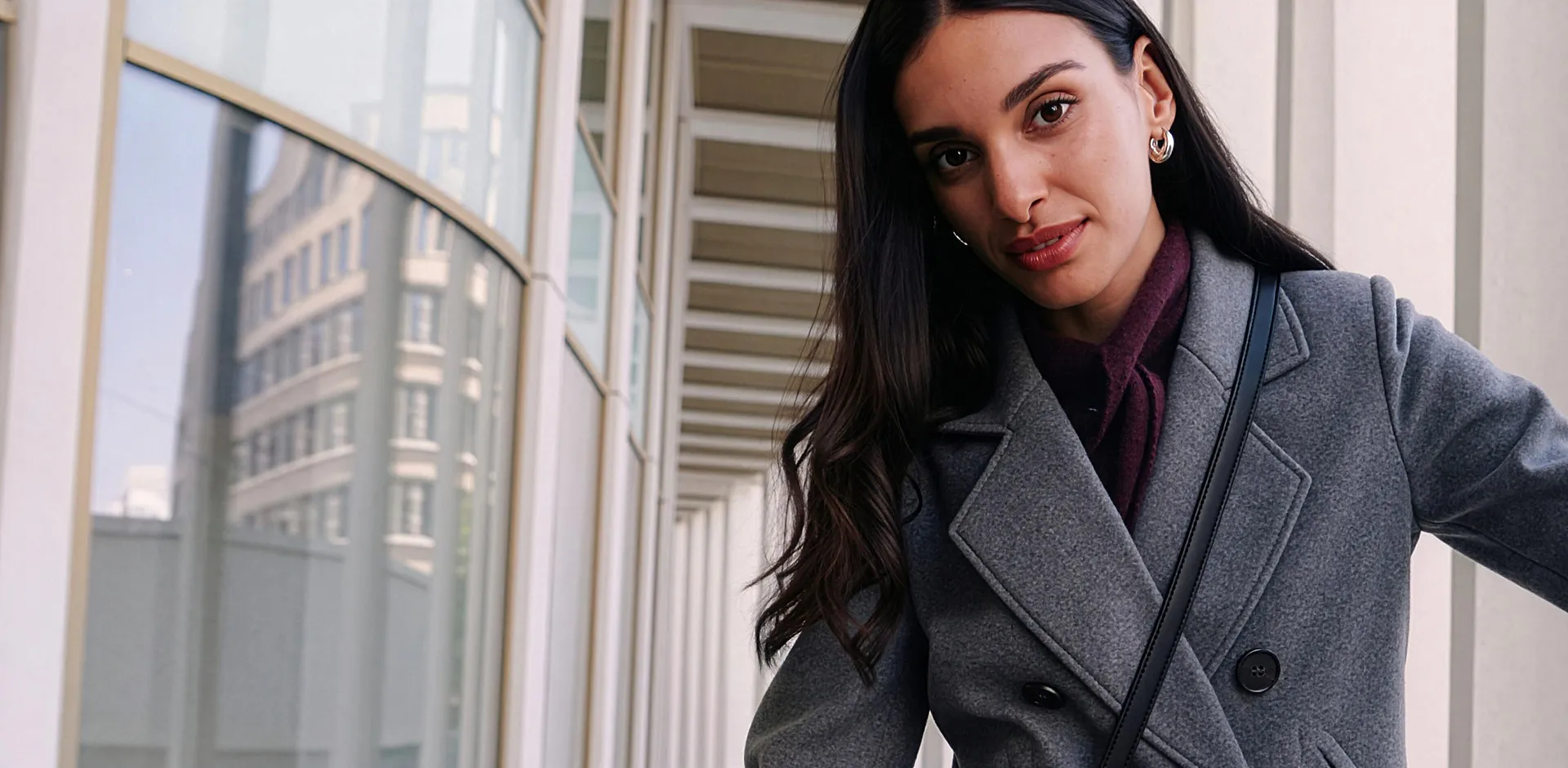Cappotto corto grigio, maglione a collo alto scuro e pantaloni bordeaux.