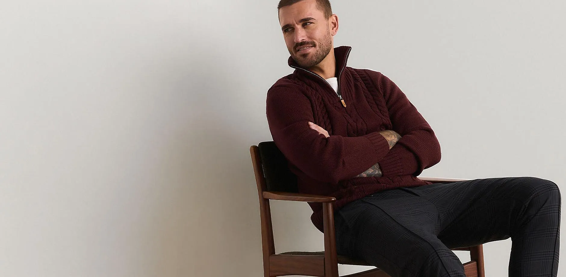 Un maglione a trecce rosso scuro con cerniera e pantaloni fantasia creano un outfit elegante.