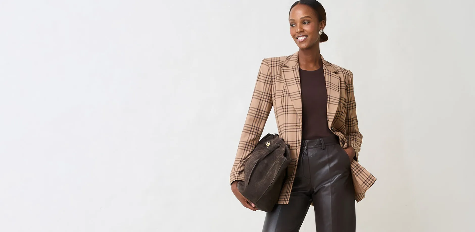 Un blazer a quadri, un top scuro, pantaloni di pelle e una borsa in camoscio creano un look elegante.