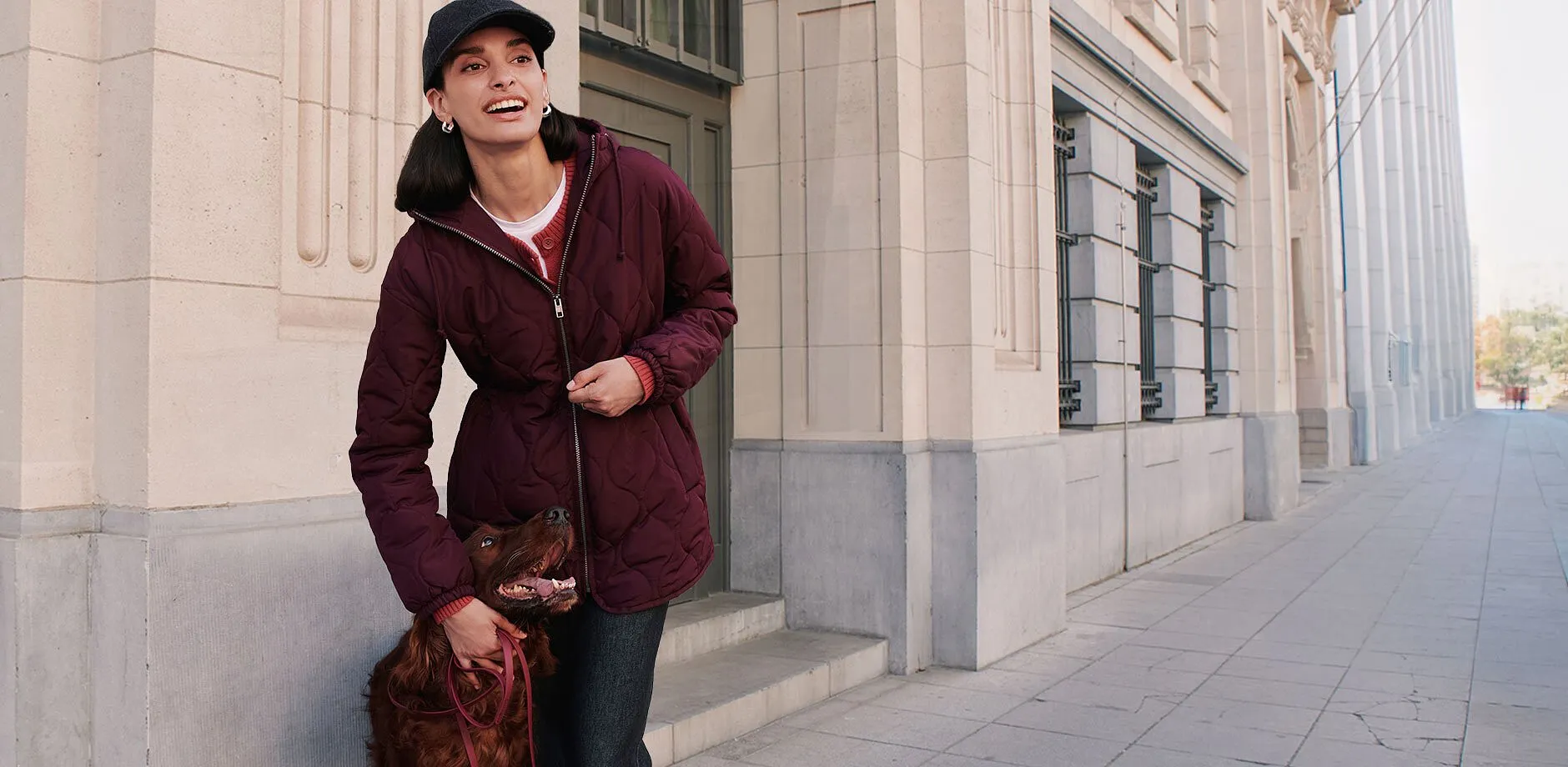 Cappellino scuro, giacca bordeaux trapuntata, cardigan rosso e jeans scuri.