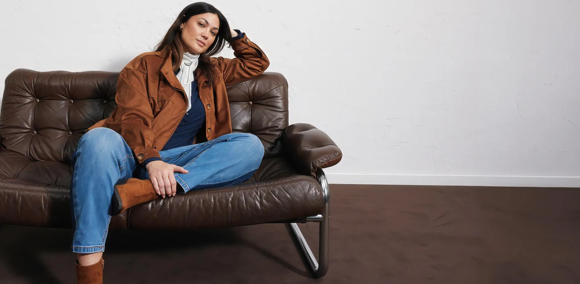 Giacca effetto pelle scamosciata, jeans blu, top scuro, sciarpa chiara e stivali.