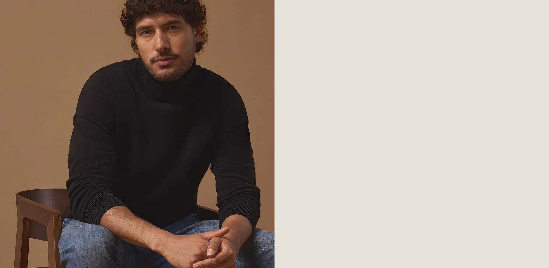 Uomo con un maglione a collo alto nero, jeans blu e stivali stringati scuri.