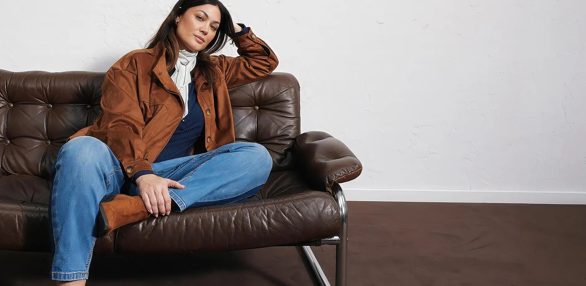 Giacca effetto pelle scamosciata, jeans blu, top scuro, sciarpa chiara e stivali.