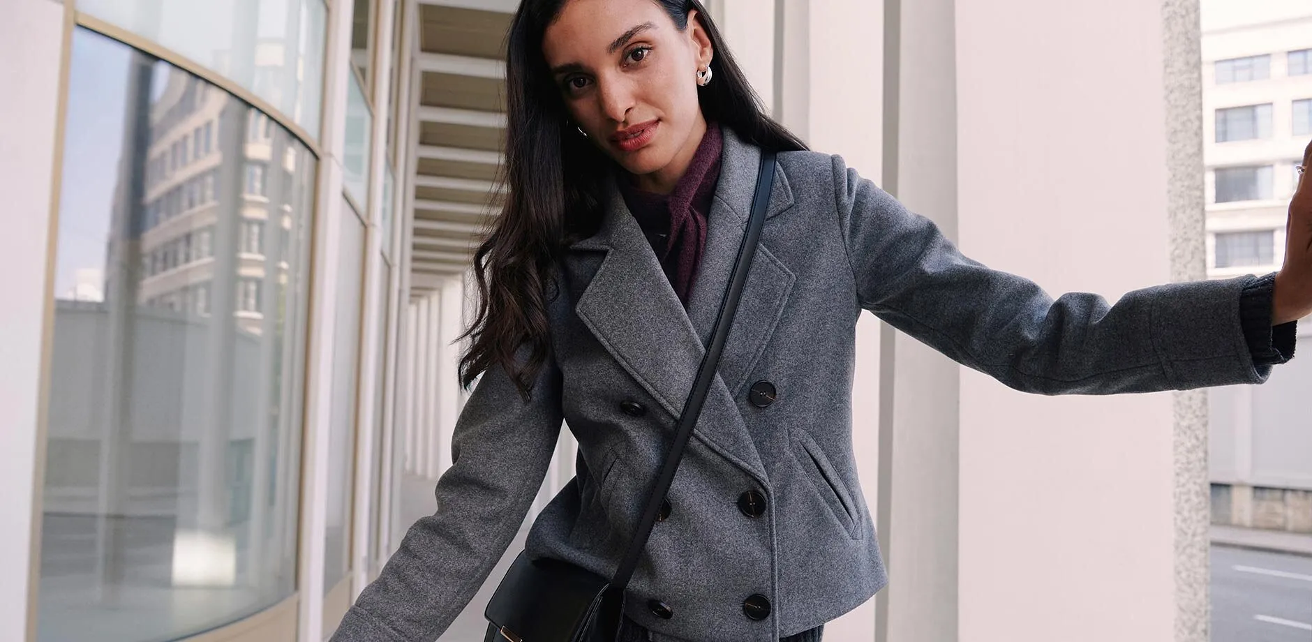 Cappotto corto grigio, maglione a collo alto scuro.