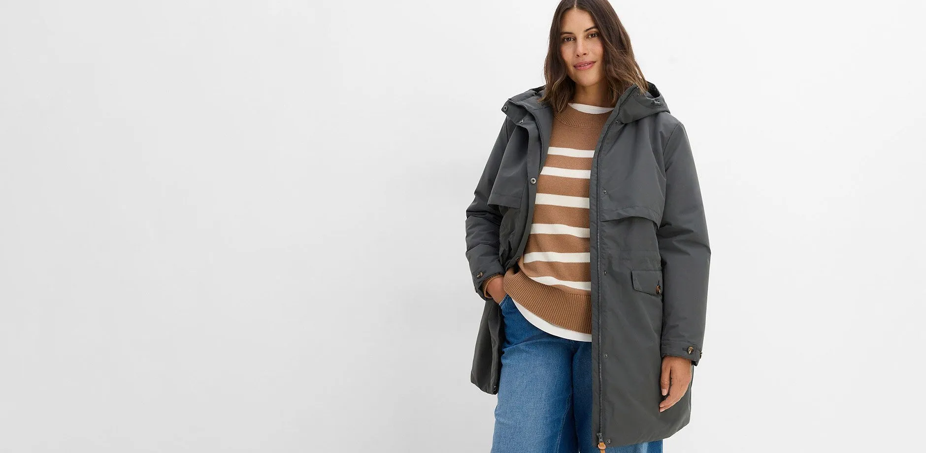 Giacca tecnica grigia, maglione a righe e comodi jeans.