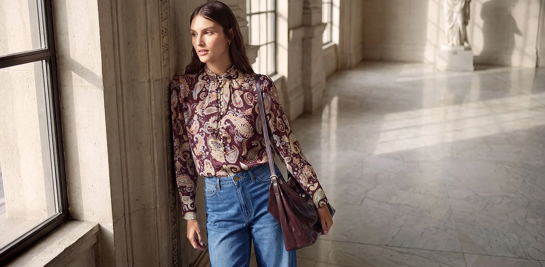 Elegante camicetta con motivo Paisley e fiocco, abbinata a jeans larghi e una borsa in pelle coordinata.