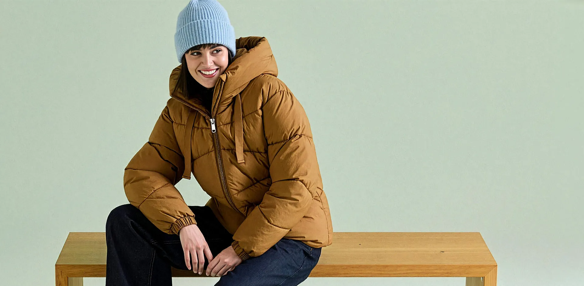 La persona indossa un berretto azzurro, una giacca trapuntata marrone e dei jeans scuri.