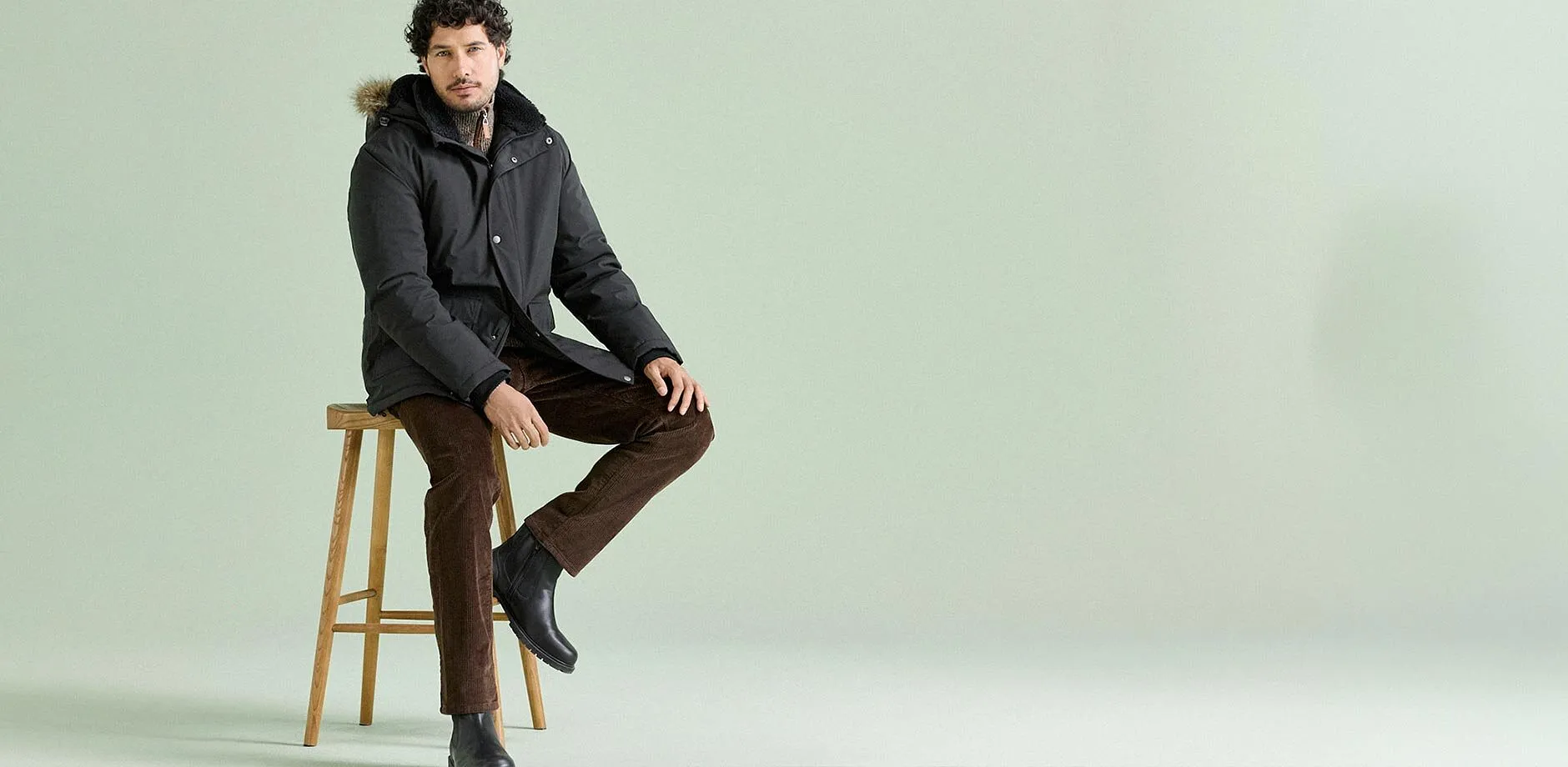 Stile invernale con un parka pesante, pantaloni di velluto a coste marroni e stivali di pelle neri.