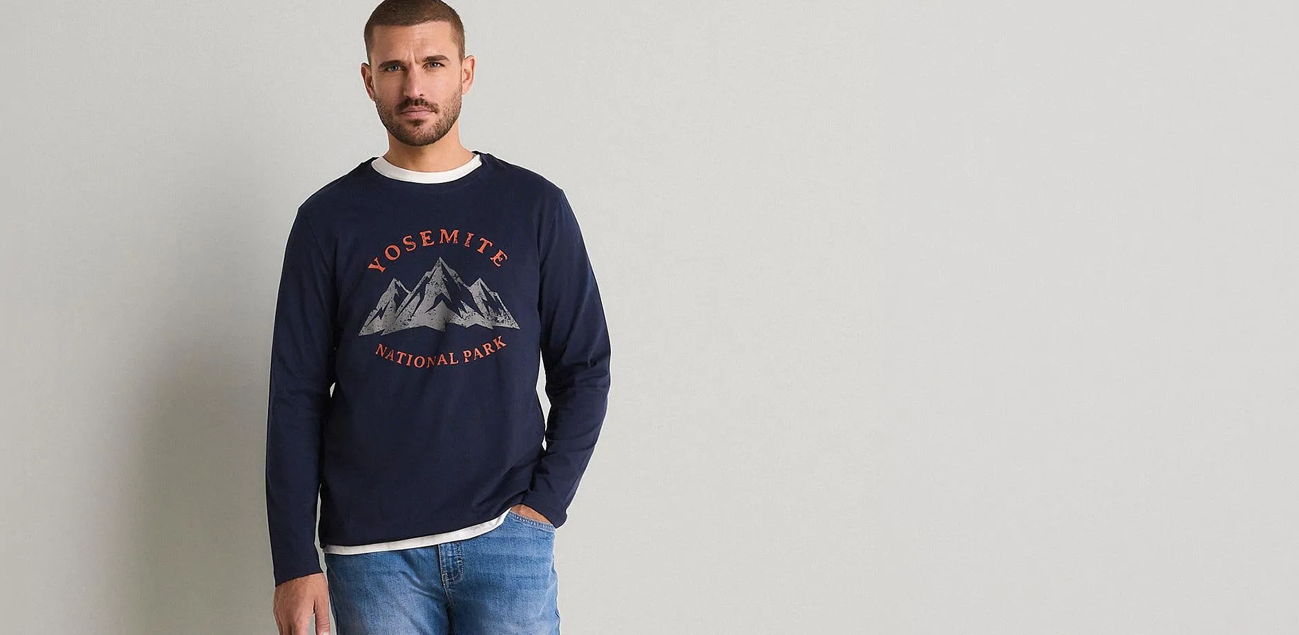 L'uomo indossa dei jeans e una maglietta a maniche lunghe blu scuro con una stampa raffigurante il Parco Nazionale di Yosemite.
