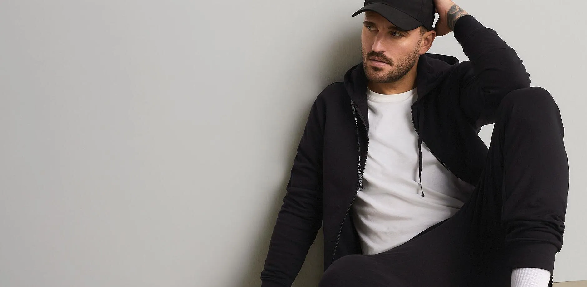 Cappellino nero, felpa con cappuccio, maglietta bianca e comodi pantaloni da jogging per un look casual.