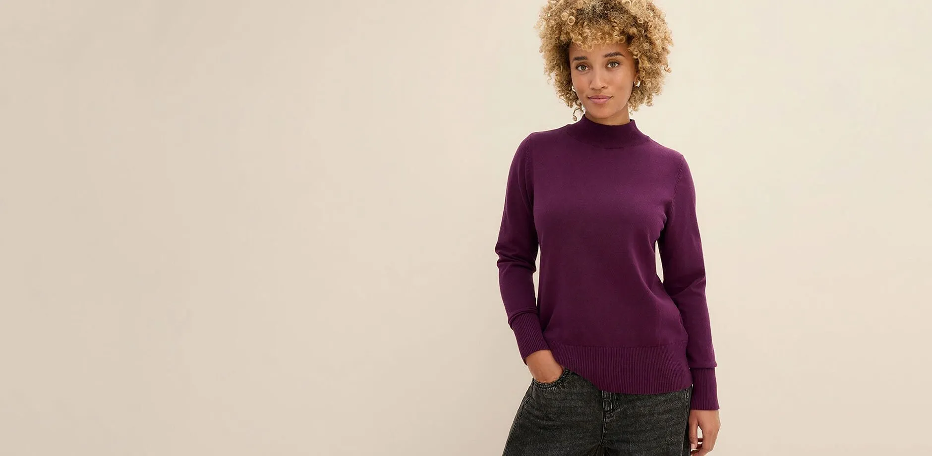 La donna indossa un maglione alla moda, viola, con collo alto e jeans scuri.