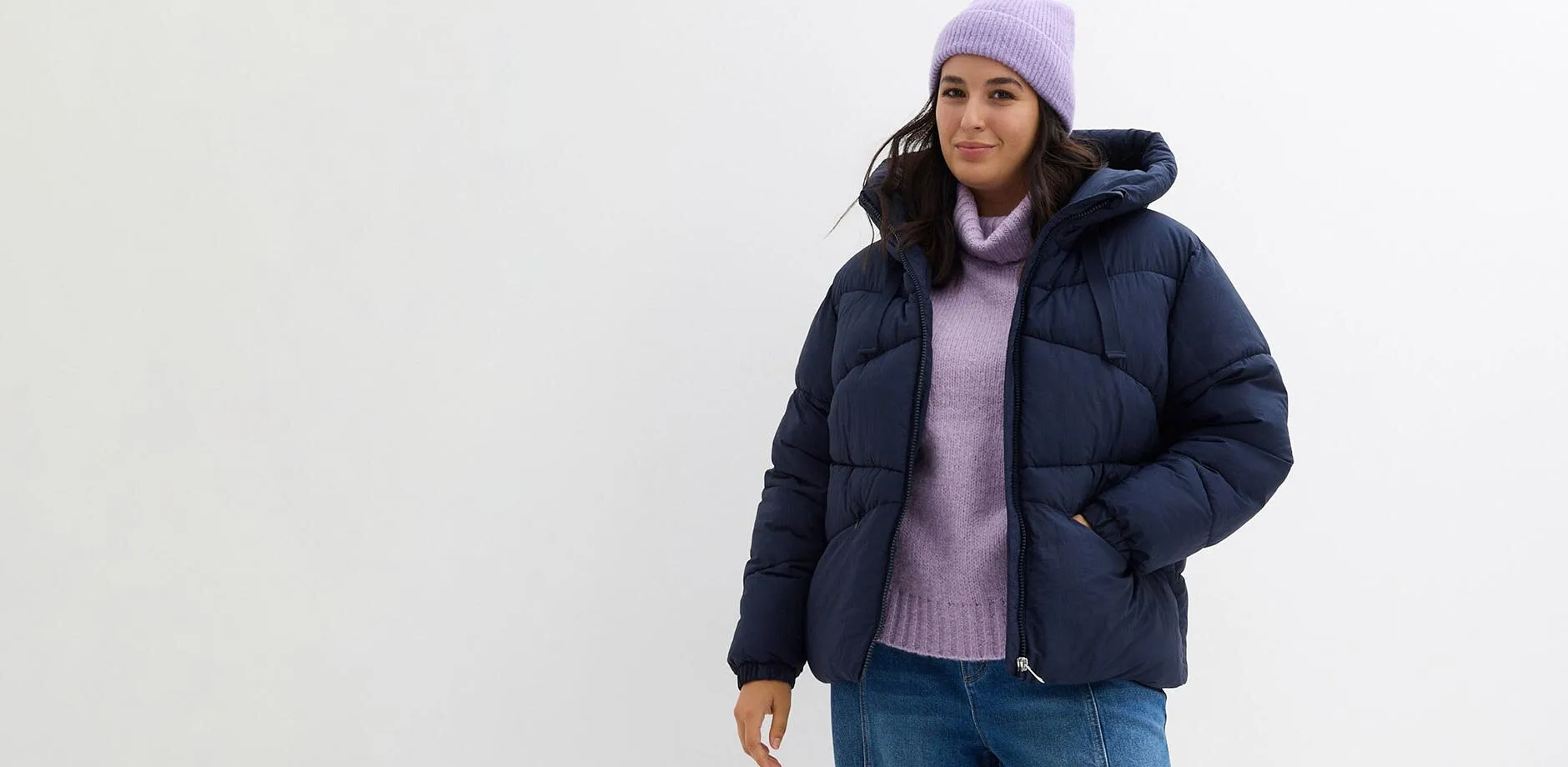Piumino blu scuro, maglione a collo alto viola e berretto di maglia.