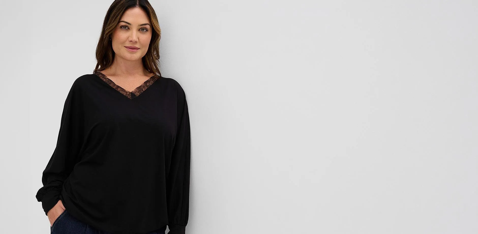 Una moderna maglia a maniche lunghe nera con un delicato pizzo sullo scollo a V, abbinata a jeans scuri.