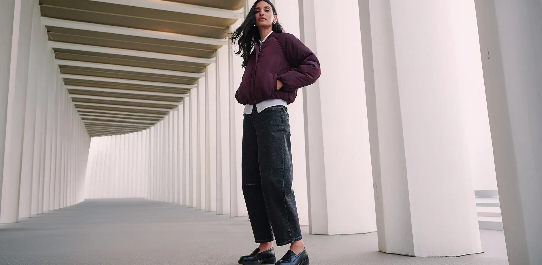 Cappellino scuro, giacca bordeaux trapuntata, cardigan rosso e jeans scuri.