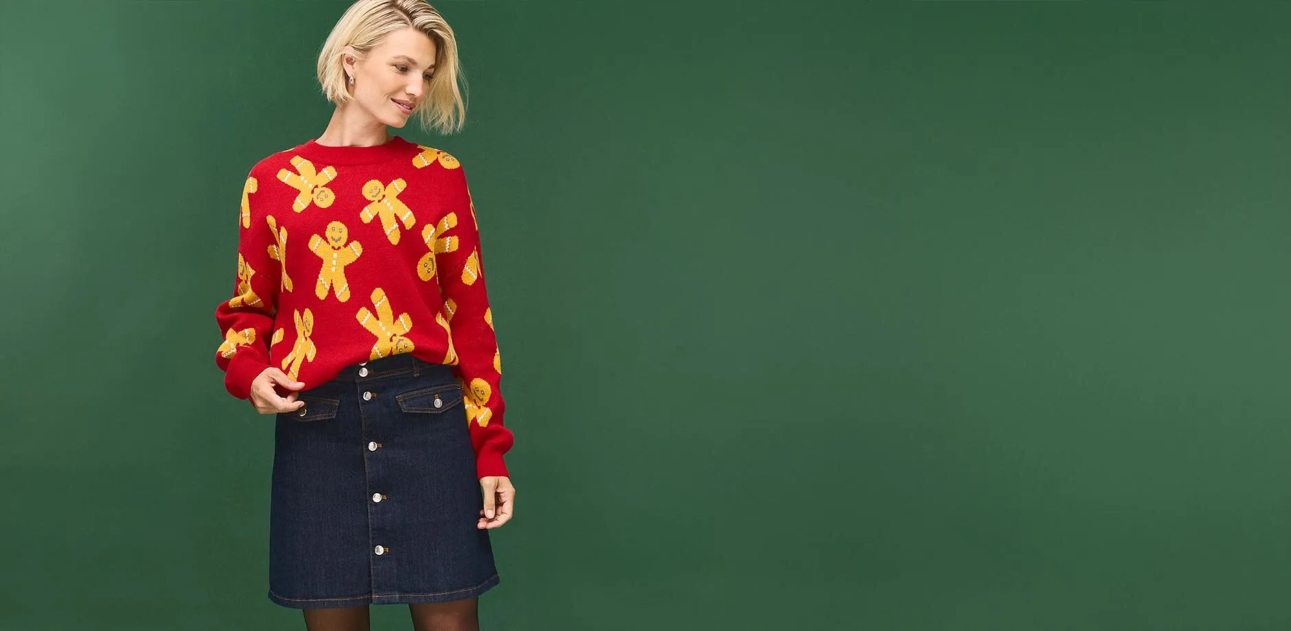 Maglione rosso con omini di pan di zenzero e gonna di jeans scura con una vistosa abbottonatura.