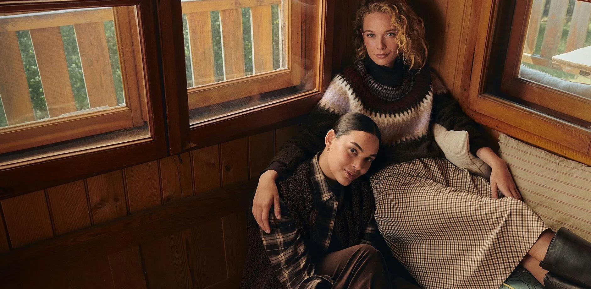 Moda autunnale confortevole: gonna a quadri, maglione fantasia, camicia e gilet scuro.