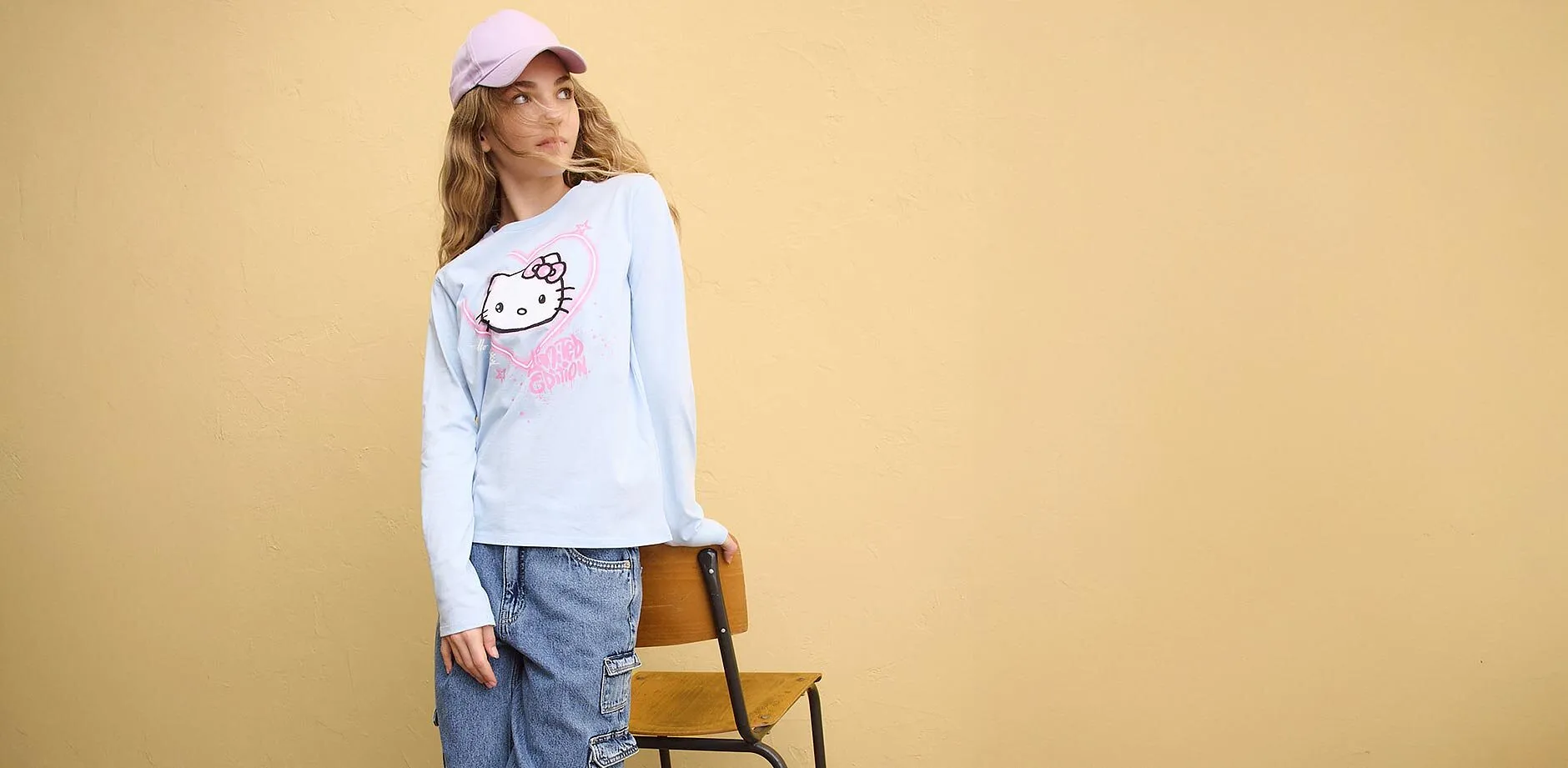 Maglietta blu a maniche lunghe con stampa Hello Kitty, jeans blu e cappellino rosa.
